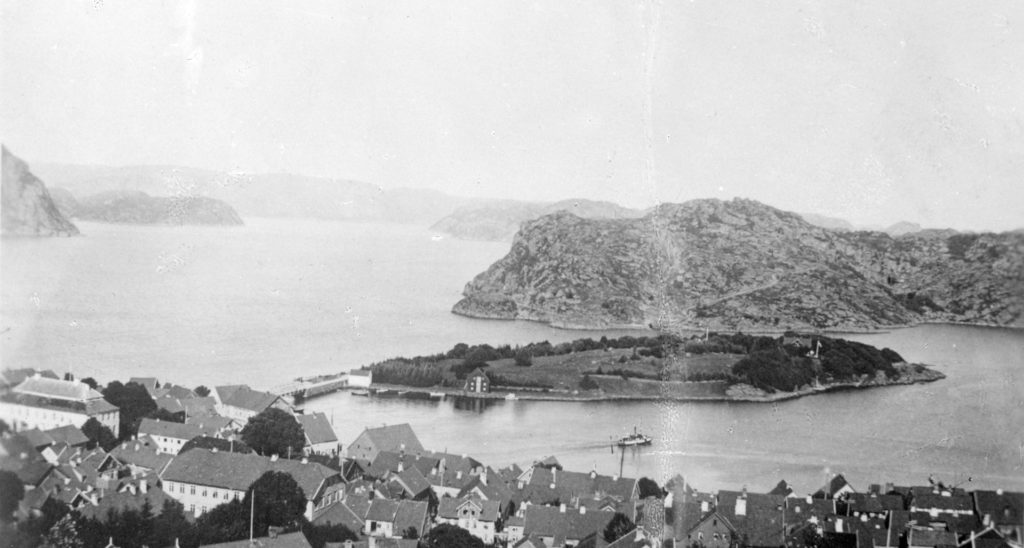 Utsikt fra Varbak mot Farøy rundt 1900 like før bybrannen i august 1901. Fra venstre på Farøy står et ishus som ble brukt til å lagre is til pakking av fisk. Den neste bygningen er et pakkhus som ble revet et par år etter siste krig. Helt til høyre ser vi familien Sundts sommerhus fra 1886. Foto: Rolf Sundt sr.
