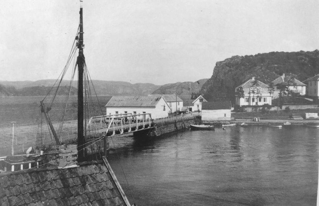 Farsund bro (1895-1958). Bildet er fra ca 1947. Fra bygningen til venstre ble det drevet med handel av kull, koks og trelast. Til høyre ser vi ishuset. Foto: Ukjent.
